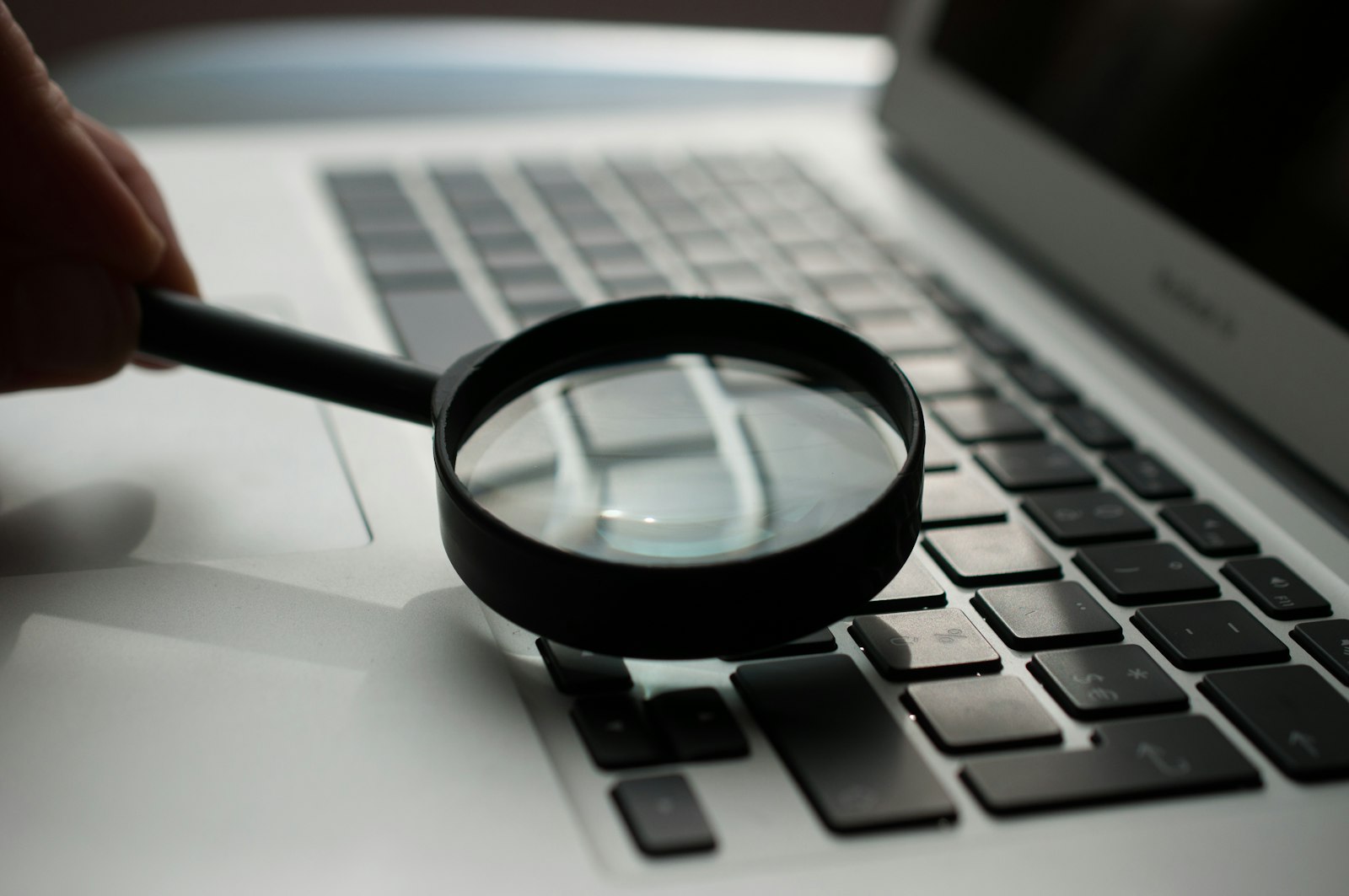 A magnifying glass held over a laptop keyboard, representing a search and research concept