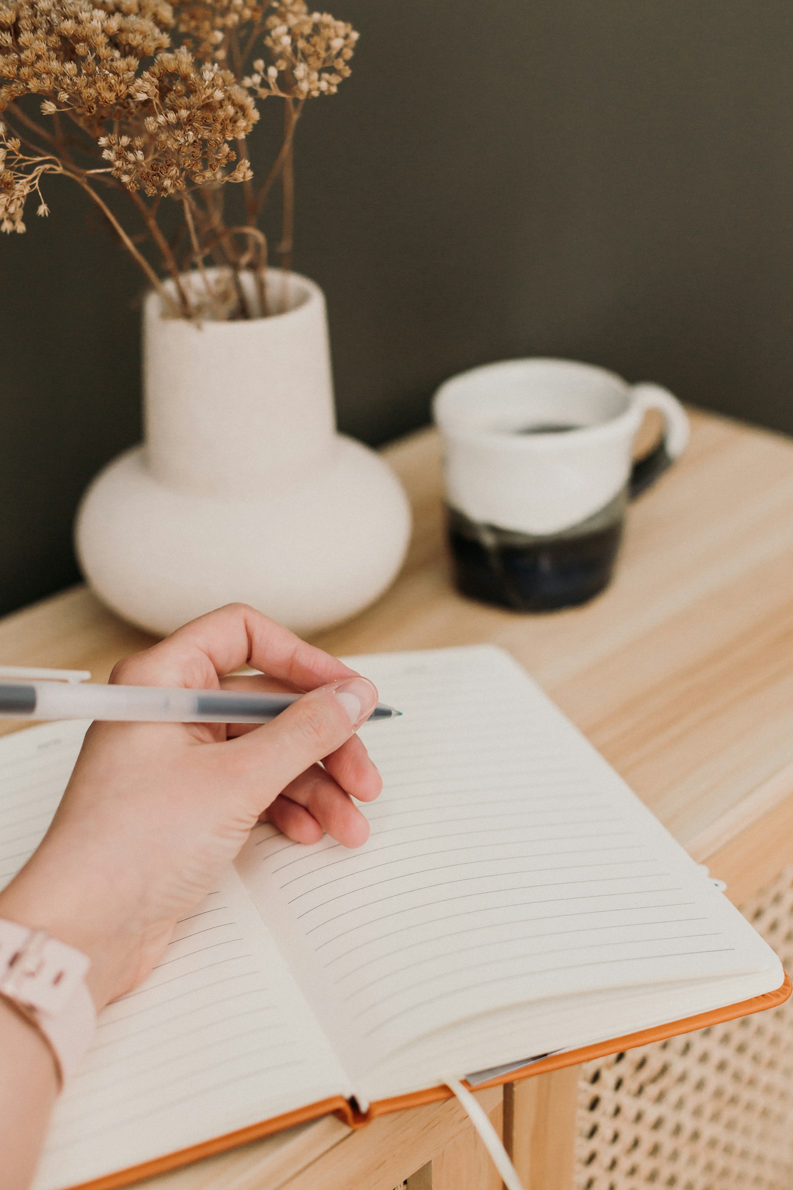 A person writing notes by hand at a desk, with a pen and notebook