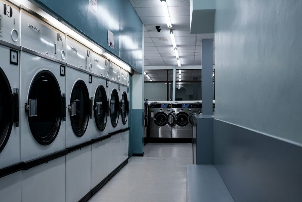 Rows of empty washing machines in a small local laundromat at night, lit by fluorescent light