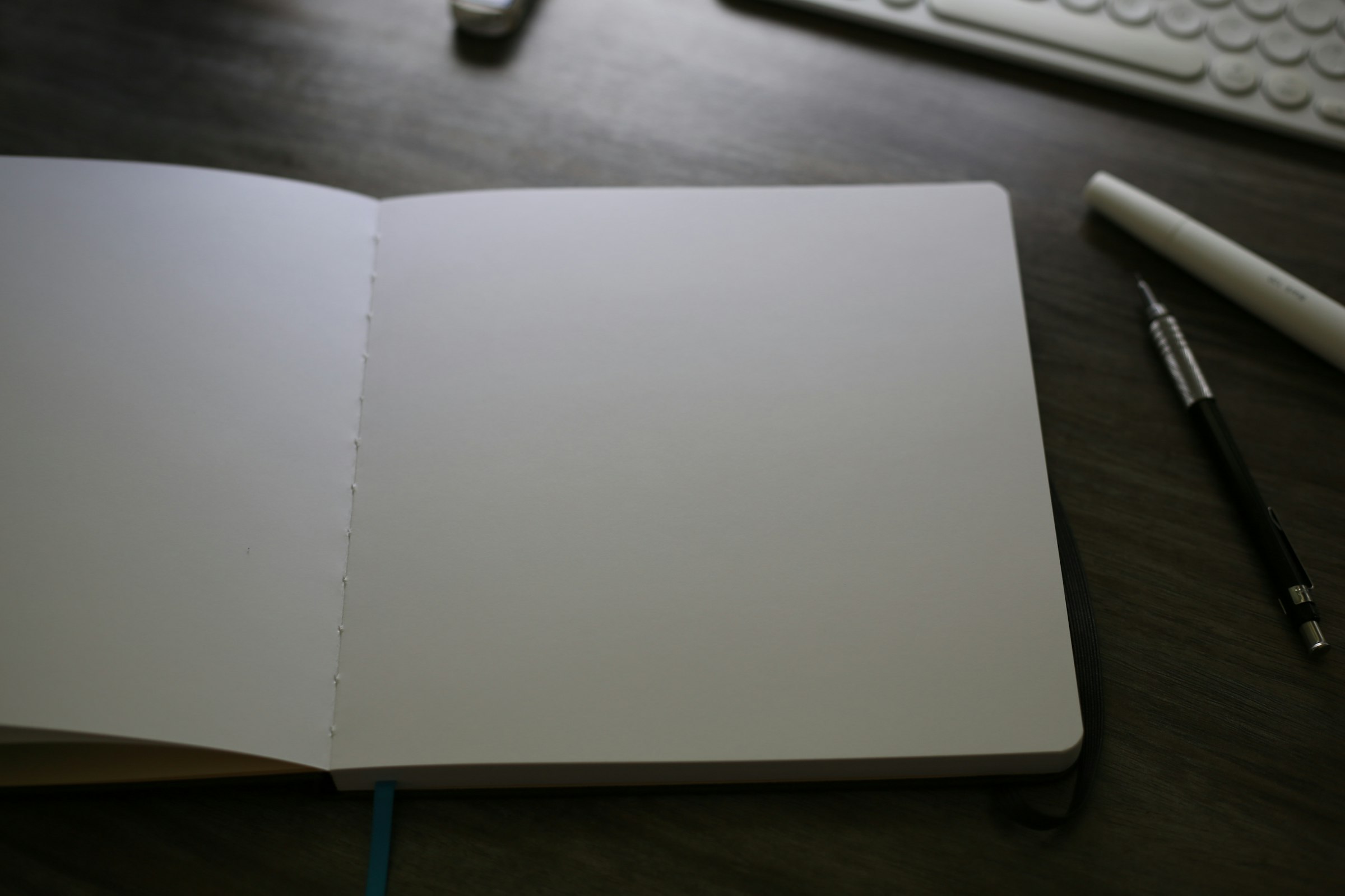 An open notebook with blank pages sitting on a desk next to a keyboard