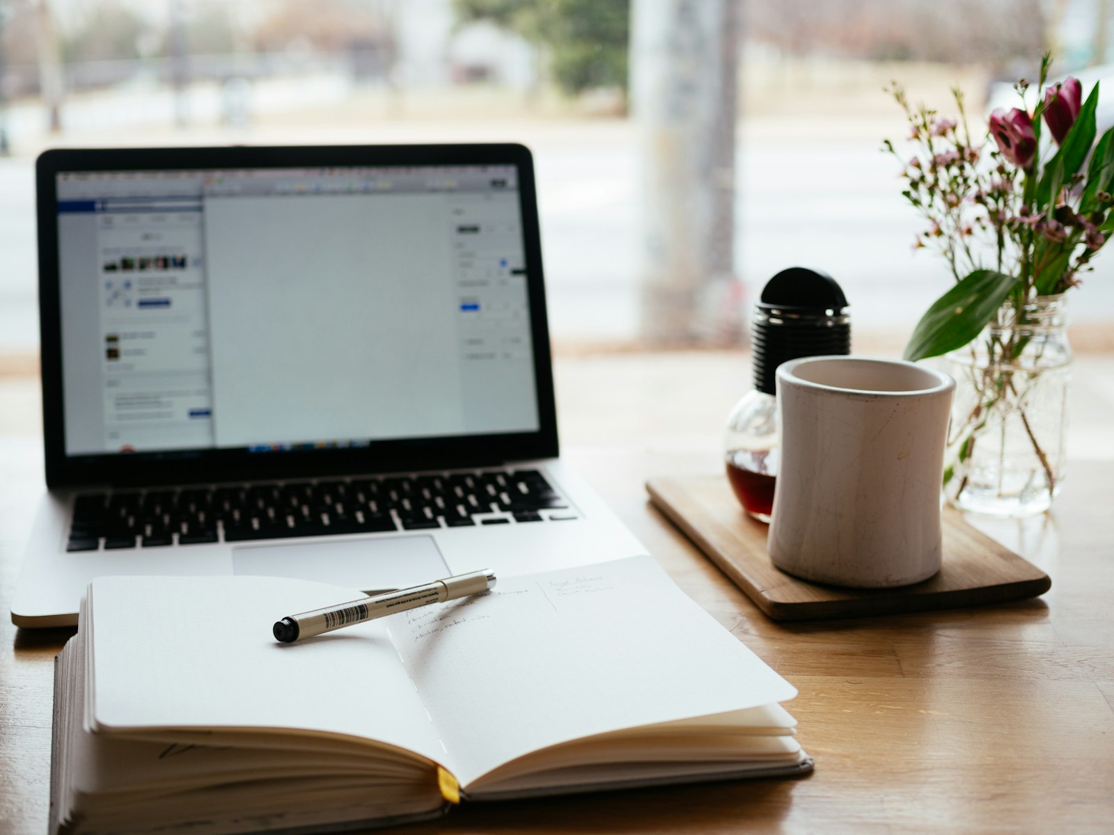 A laptop and open notepad on a desk, representing the drafting stage of essay writing